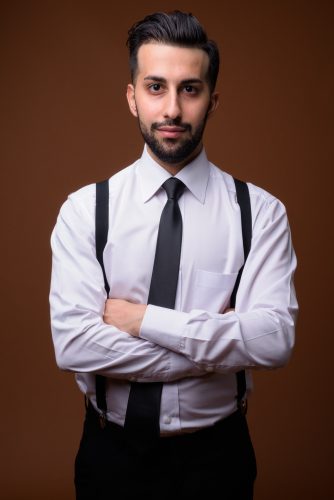 Young handsome bearded Iranian businessman against brown backgro